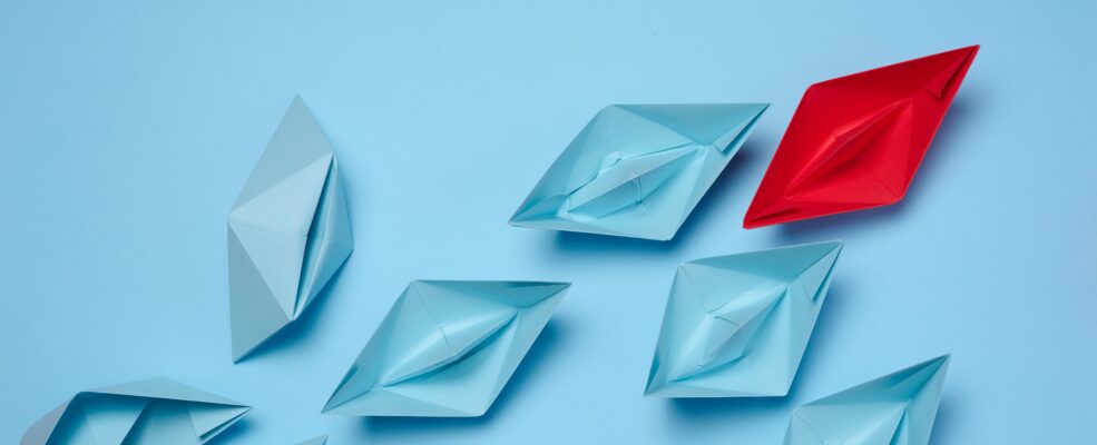 Blue paper boats following a red one as a metaphor for standing out from the crowd