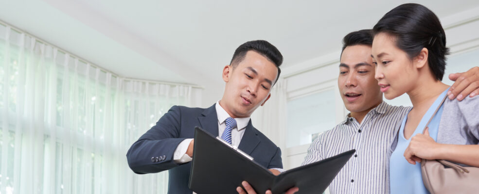 A salesman gestures at a folder to two clients. They all look pleased with what he's selling