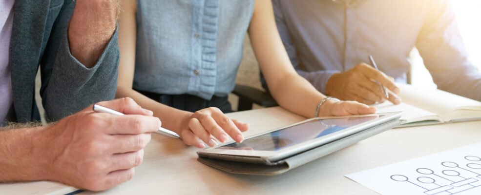 Cropped image of coworkers discussing business plan on tablet computer during meeting