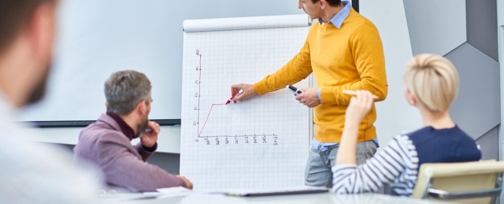 People discussing a marketing plan. One man draws graph paper while others watch