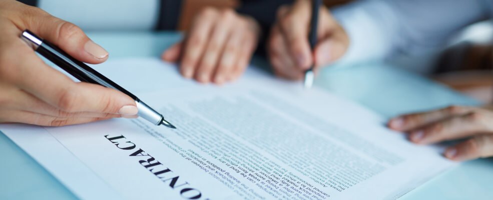 Closeup shot of two business partners signing contract at meeting: woman pointing and man putting signature below text