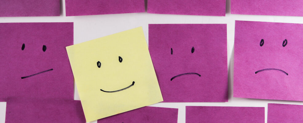 One yellow post-it note with a smiley face drawn on is among several frowning post it notes to illustrate your brand standing out.